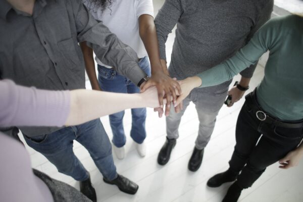 From above of faceless diverse coworkers wearing casual outfits stacking hands together while gathering in modern office at daytime