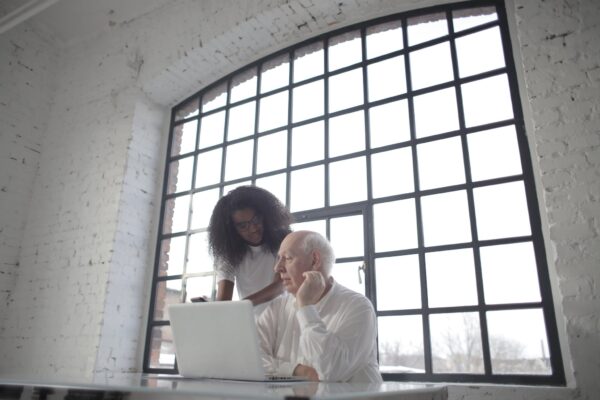 Professional aged male entrepreneur discussing startup project with young female African American colleague during office work with laptop and smartphone in workplace with industrial interior